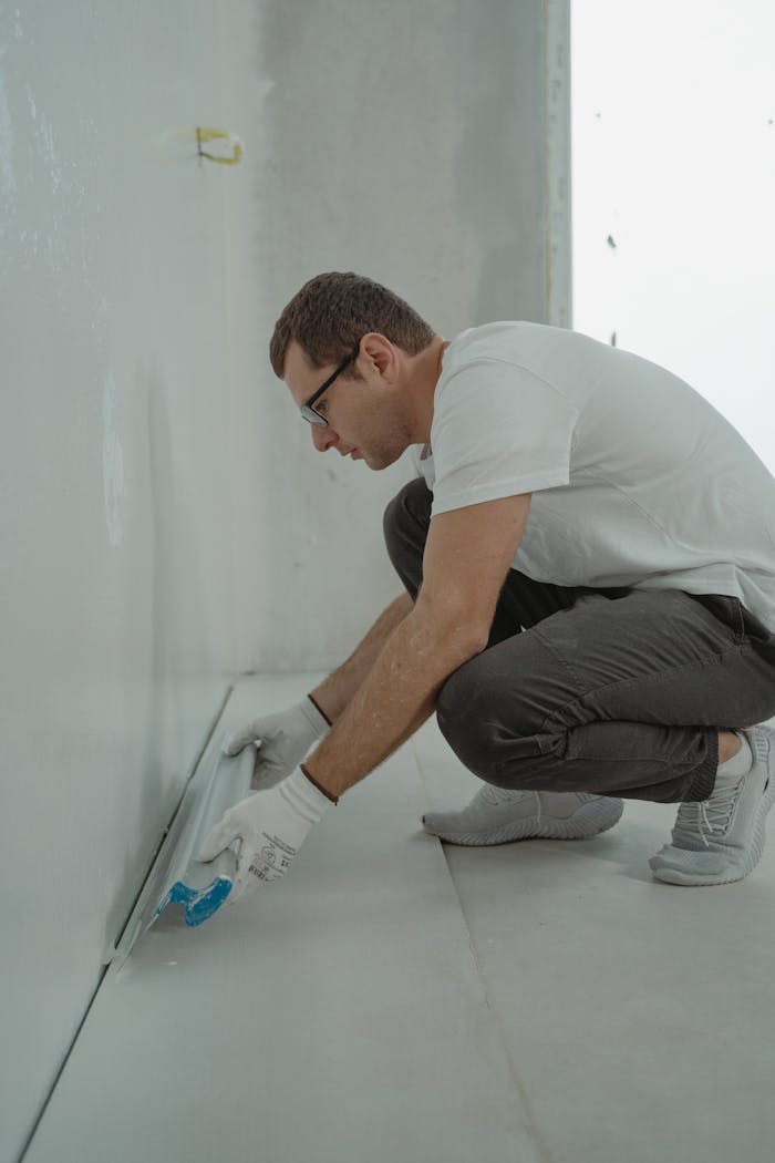 A man wearing casual attire working on a home renovation project indoors with painting tools.